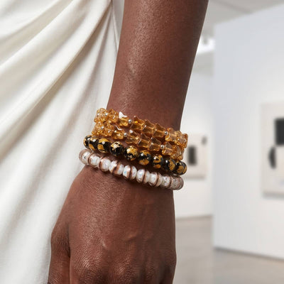 NOGU MoMA Art II stacked beaded bracelets in amber, black-and-gold, and pearly white tones, styled in a gallery setting.