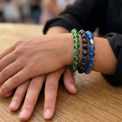NOGU Made to Pair Pitch Black collection with layered green, black and blue firefly glass bead bracelets on a wrist.