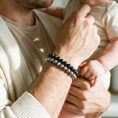 Father wearing stacked black and silver beaded bracelets while holding a baby, a meaningful Father’s Day gift.