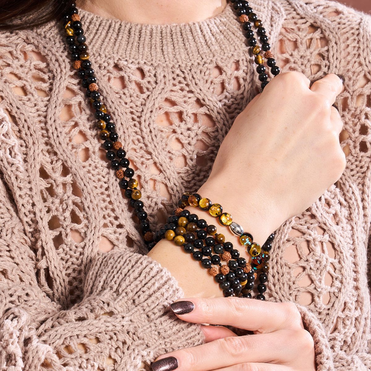 NOGU multi-strand black and amber beaded necklace styled as layered bracelets over a blush open-knit sweater.