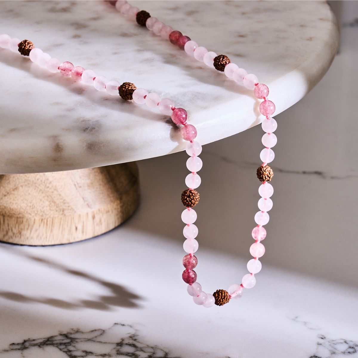 Pink gemstone beaded necklace with pale rose round beads, deeper pink accents, and textured dark brown seed beads.