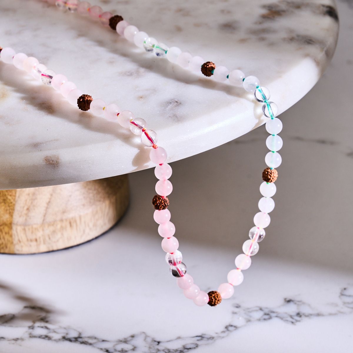 Pastel pink and white beaded necklace with clear glass accents, brown textured beads, and colorful thread details.