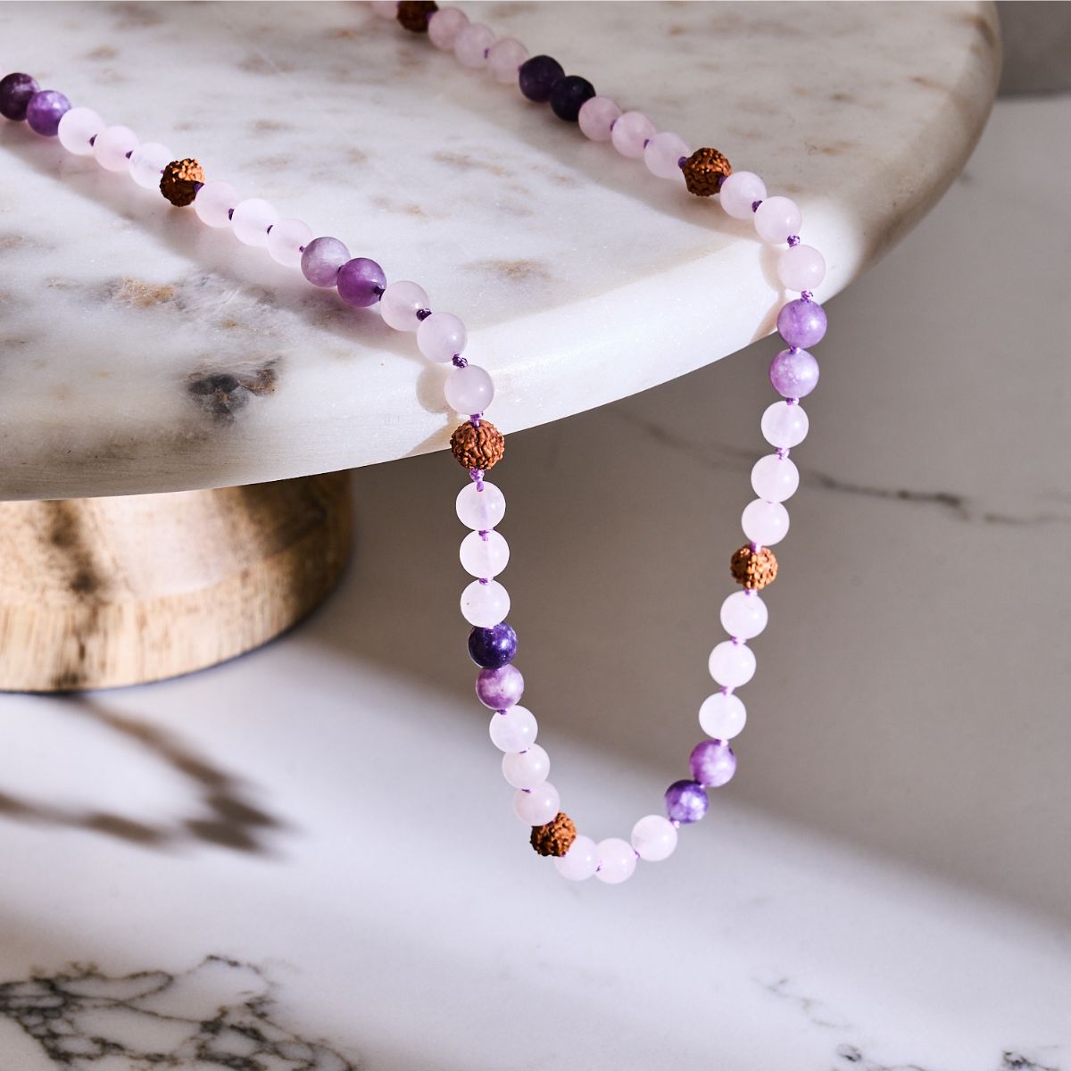 NOGU beaded necklace with pale pink and purple gemstone beads, accented by textured brown seed beads.