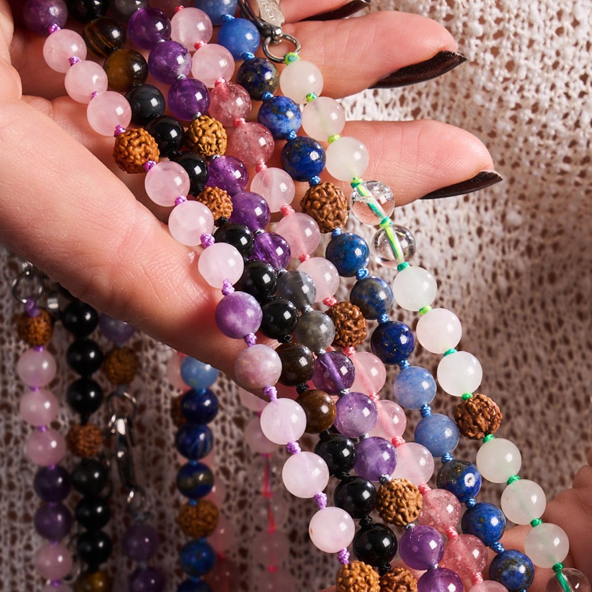 Colorful gemstone bead necklaces with pink, purple, blue, black and clear stones, held against a textured knit top.