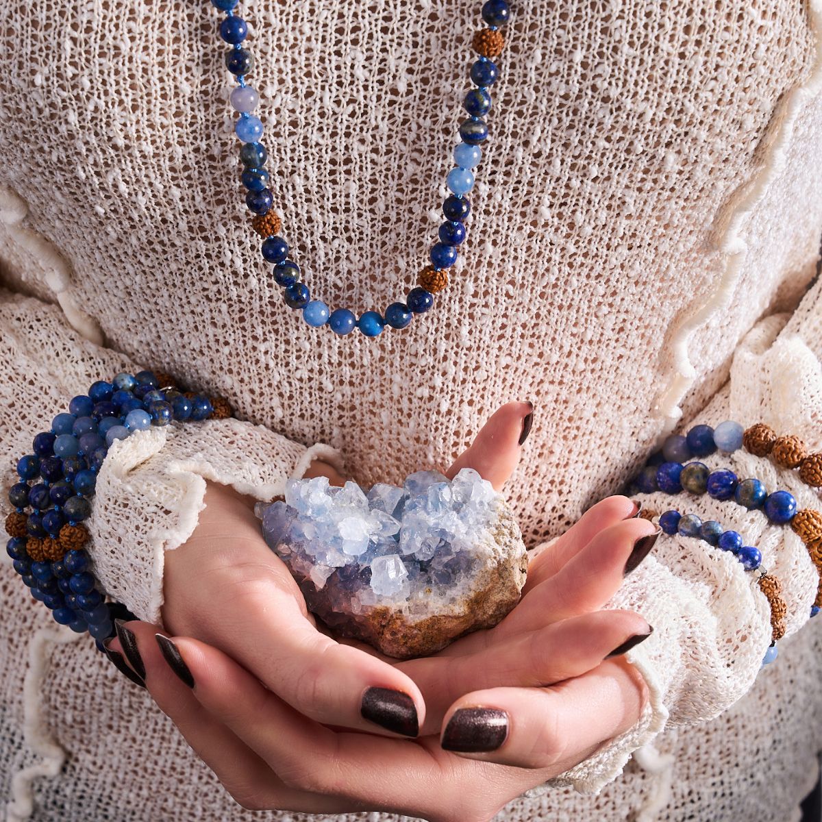 NOGU blue beaded gemstone necklace and matching bracelets styled with a pale blue crystal cluster on a cream knit sweater.