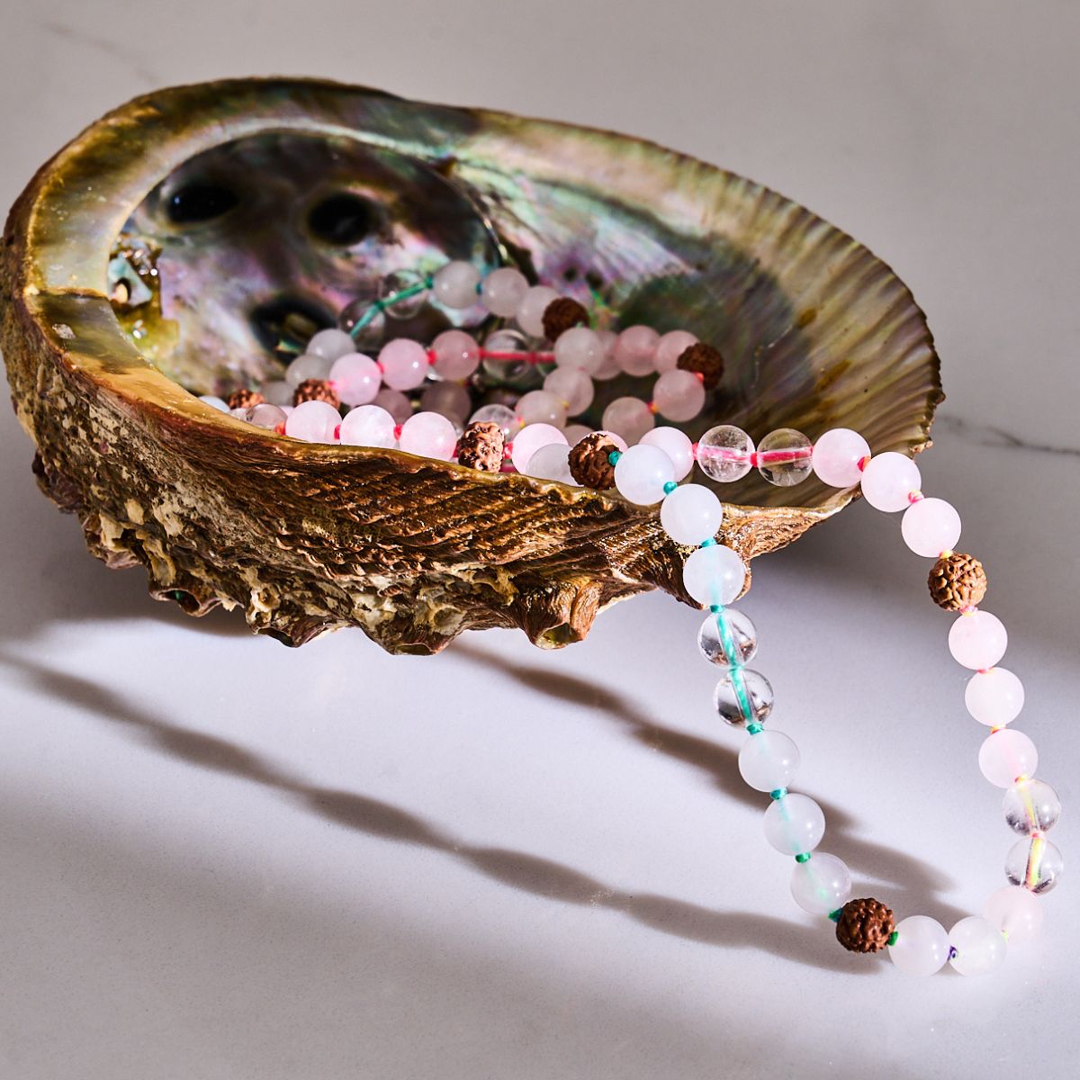 Pastel pink and clear beaded necklace with textured brown seed beads, draped in an iridescent abalone shell.