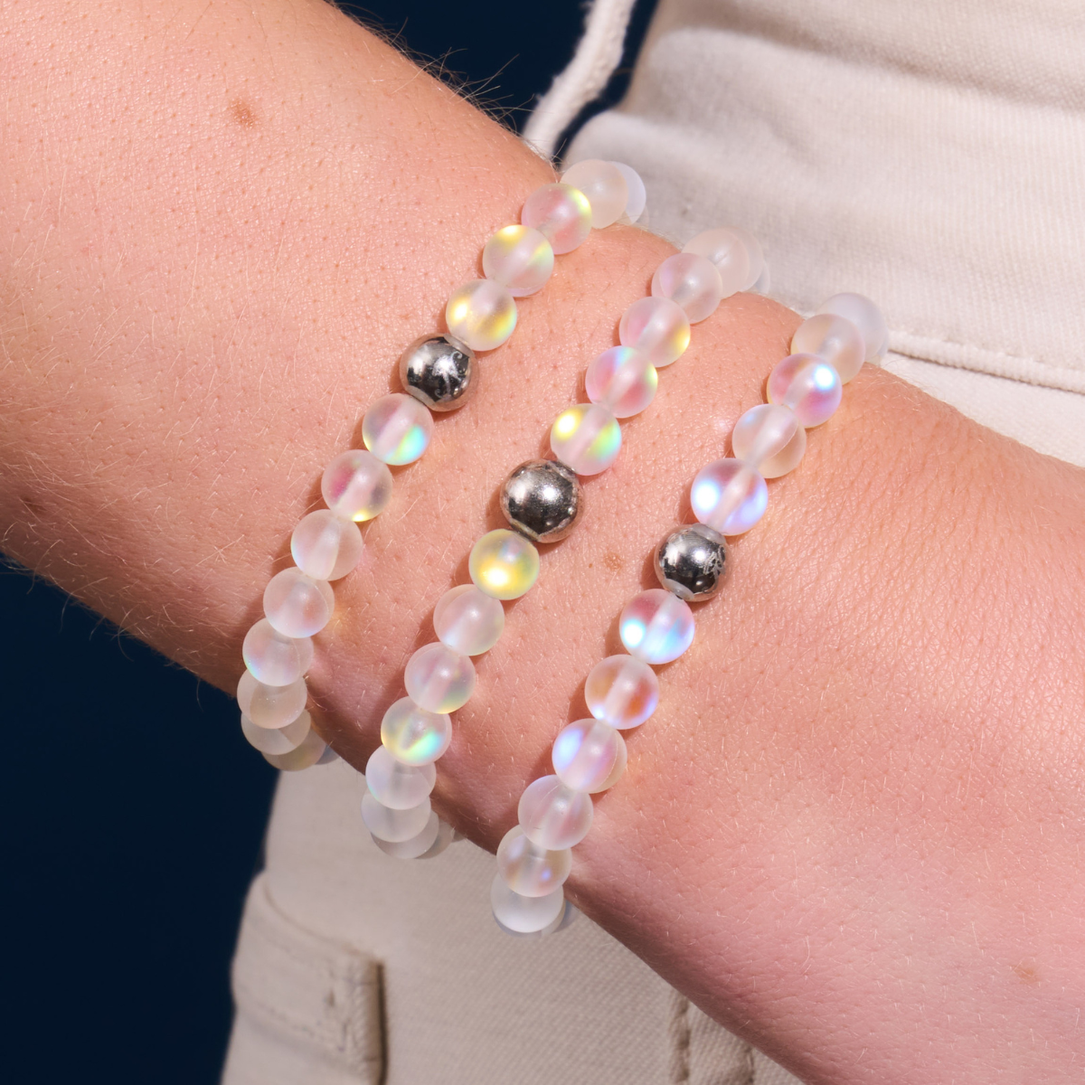 Three translucent frosted beaded bracelets with iridescent rainbow sheen and polished silver-tone accent beads, layered on a wrist.