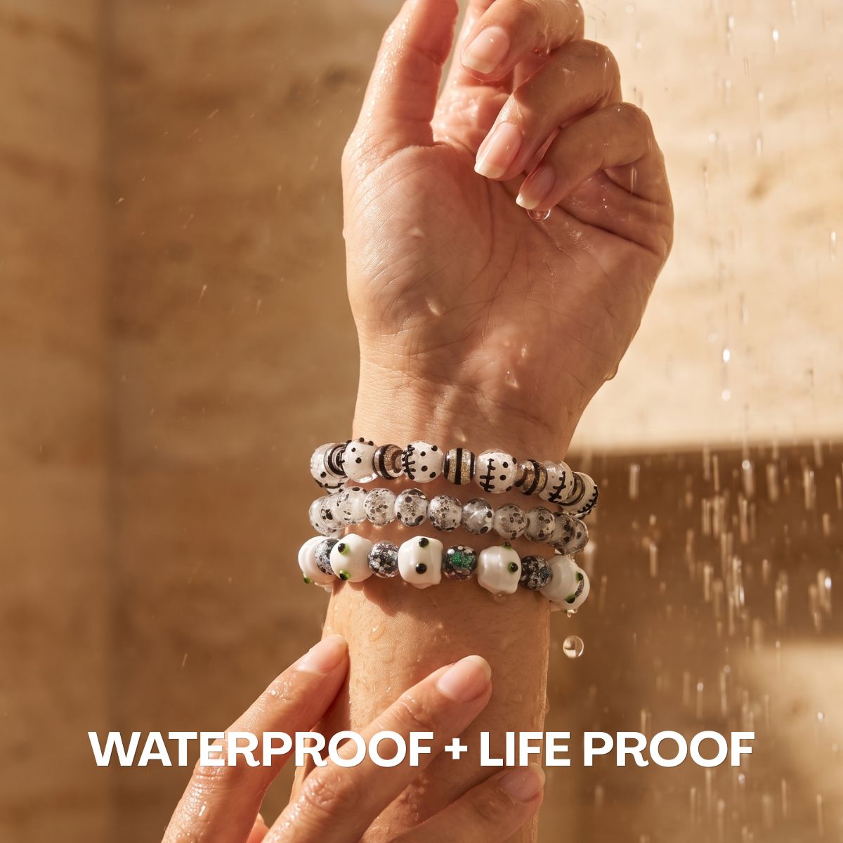 Stack of white and black patterned beaded bracelets with green accents worn on a wrist under running water.