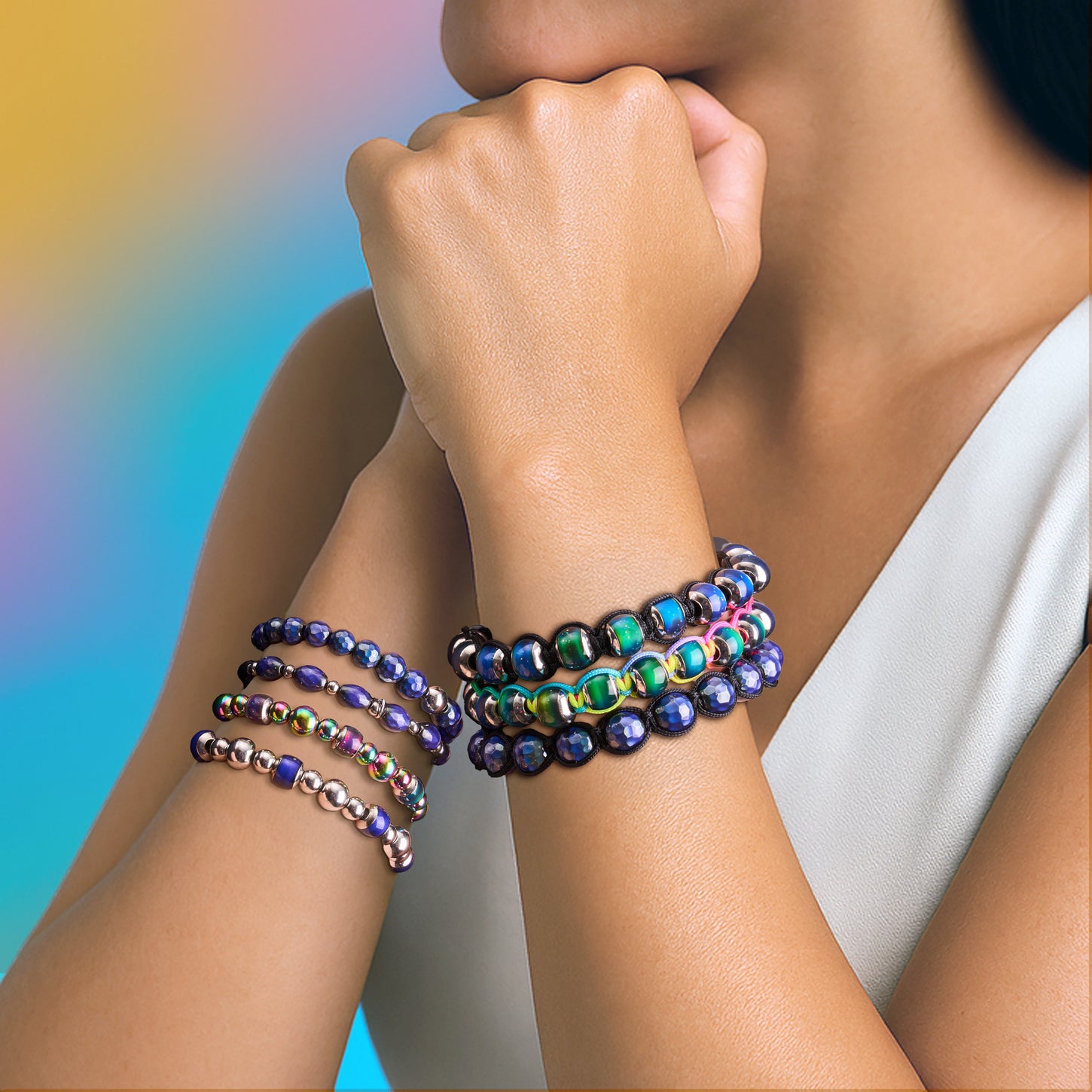 Model wearing stacked stretch bead bracelets in iridescent green, purple, blue and silver tones with black accents.