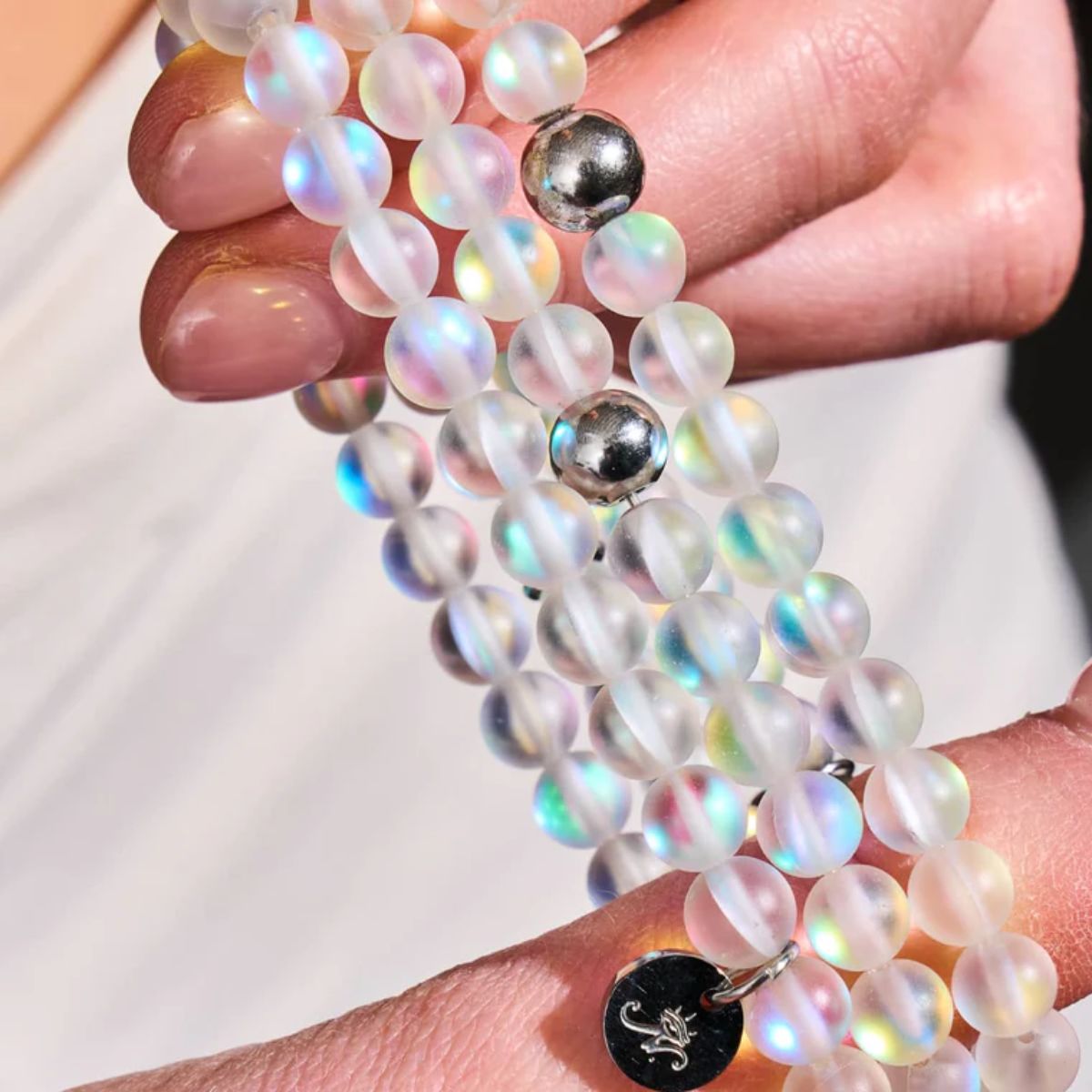 Iridescent frosted bead bracelet with polished silver-tone spacer beads and a small round engraved charm.
