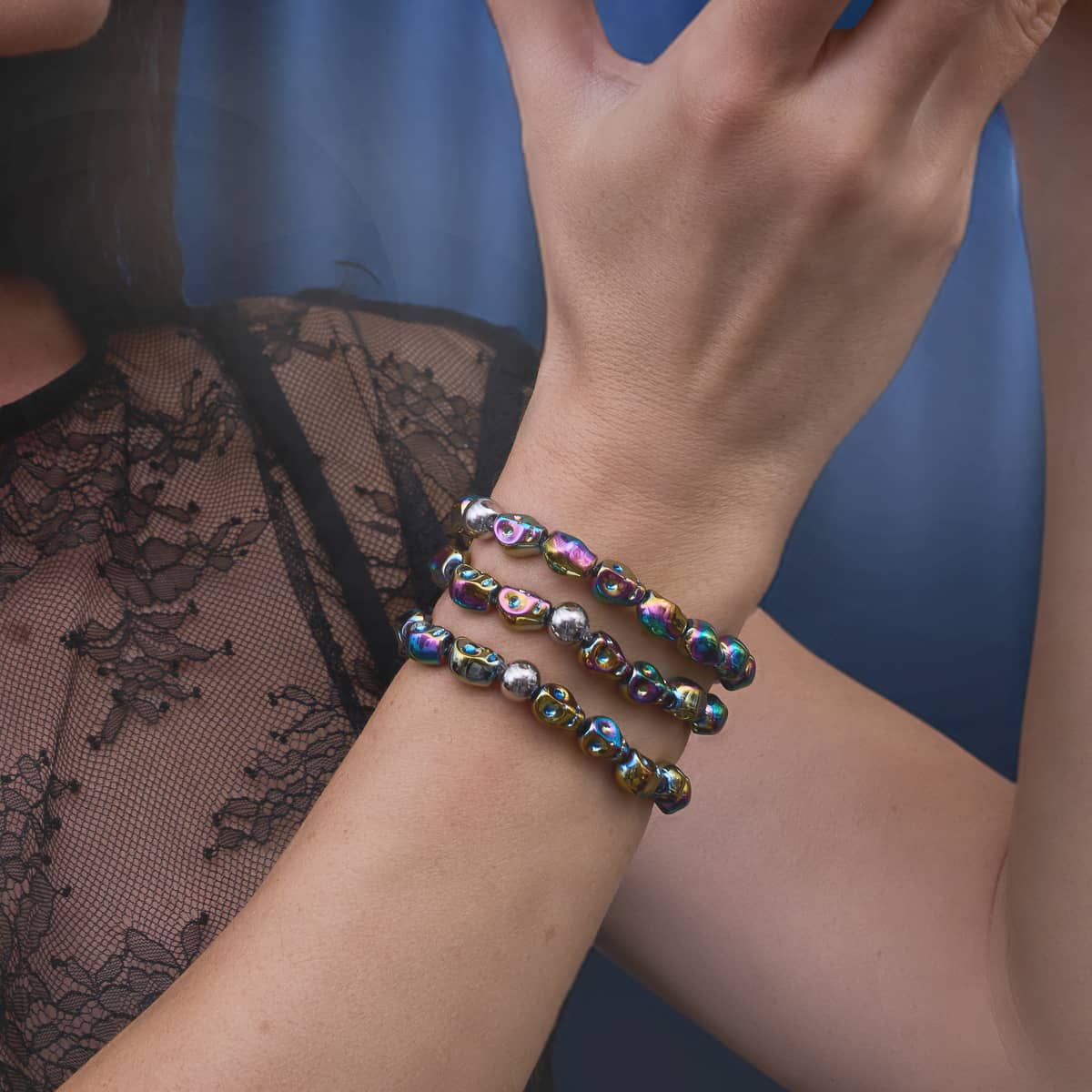 Stacked iridescent metallic bead bracelets with silver-toned round accents, styled on a wrist with a black lace top.