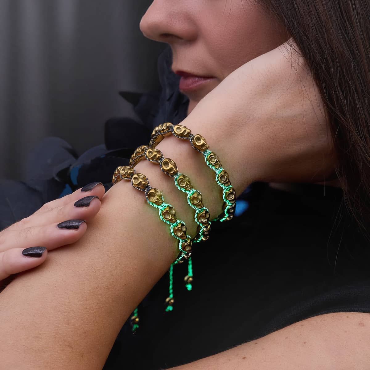 Layered gold-tone skull bead bracelets with vivid green braided cord ties, styled on a wrist.