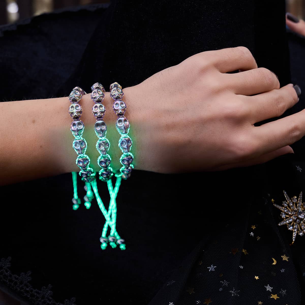 Three iridescent silver skull bead bracelets with glowing turquoise adjustable cords worn on a wrist.