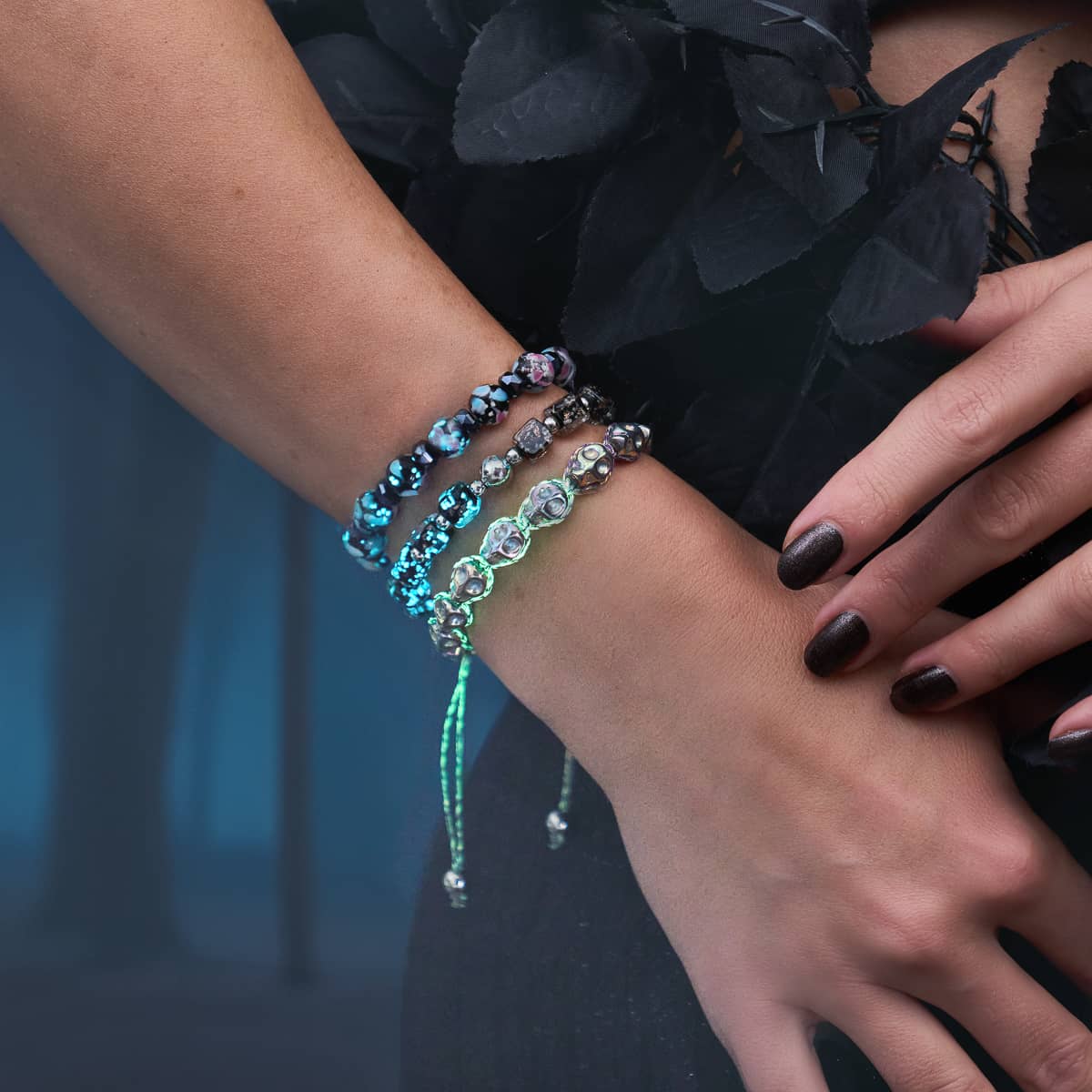 Stacked beaded bracelets with iridescent floral glass beads and teal crystal accents, worn with black floral styling.