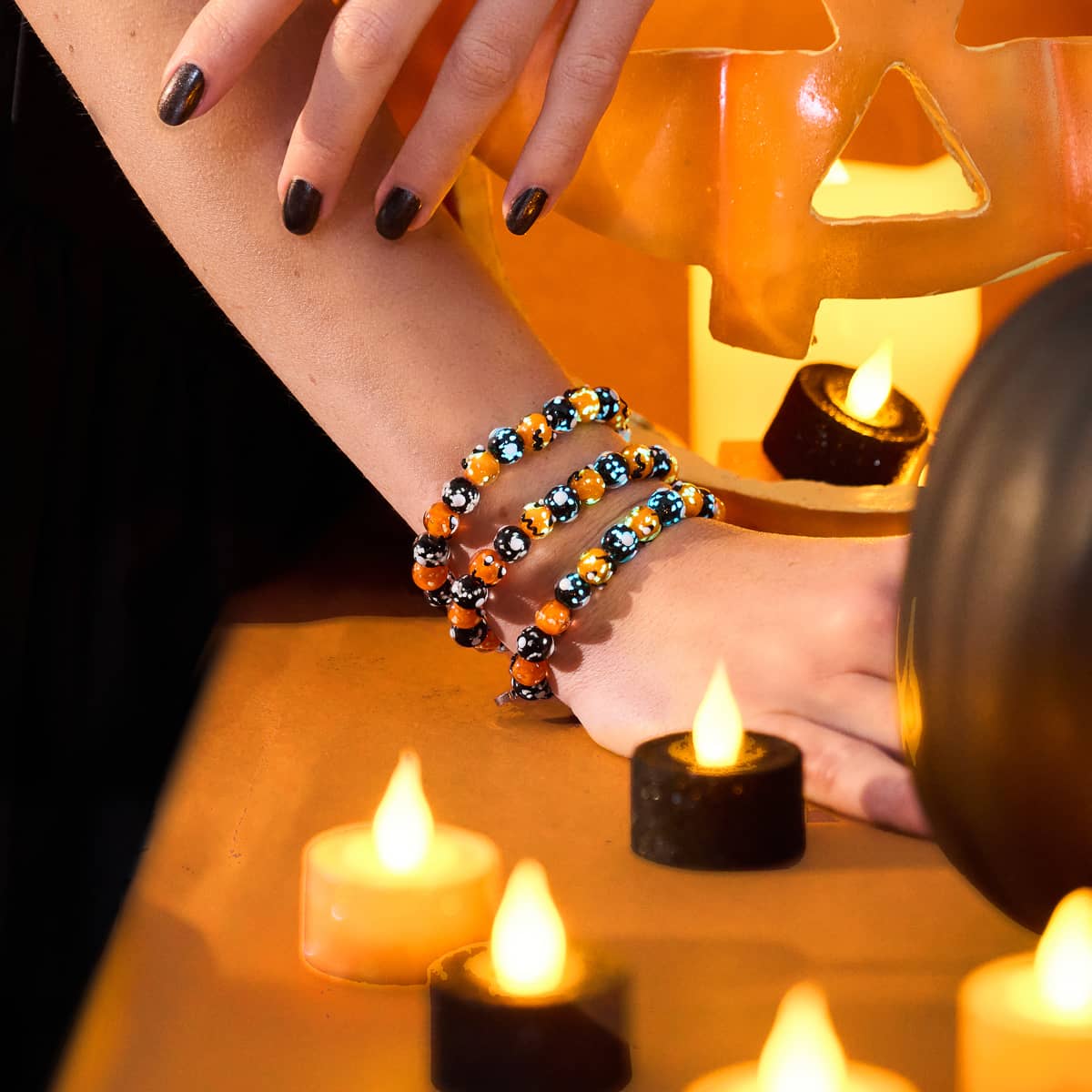 Midnight Pumpkin bracelet with glowing orange and black Firefly Glass beads worn on wrist near Halloween decorations by NOGU