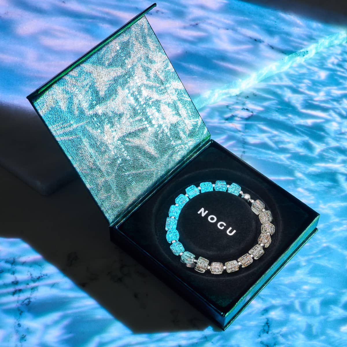 Alabaster Firefly Glass Pebble Bracelet glowing blue and clear cube beads in silver box with NOGU logo by NOGU