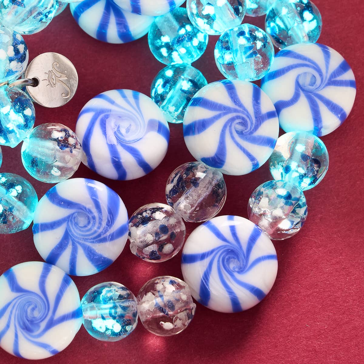 Blue Gumdrop bracelet close-up showing glowing blue spiral gumdrop beads and clear firefly glass beads on red background by NOGU