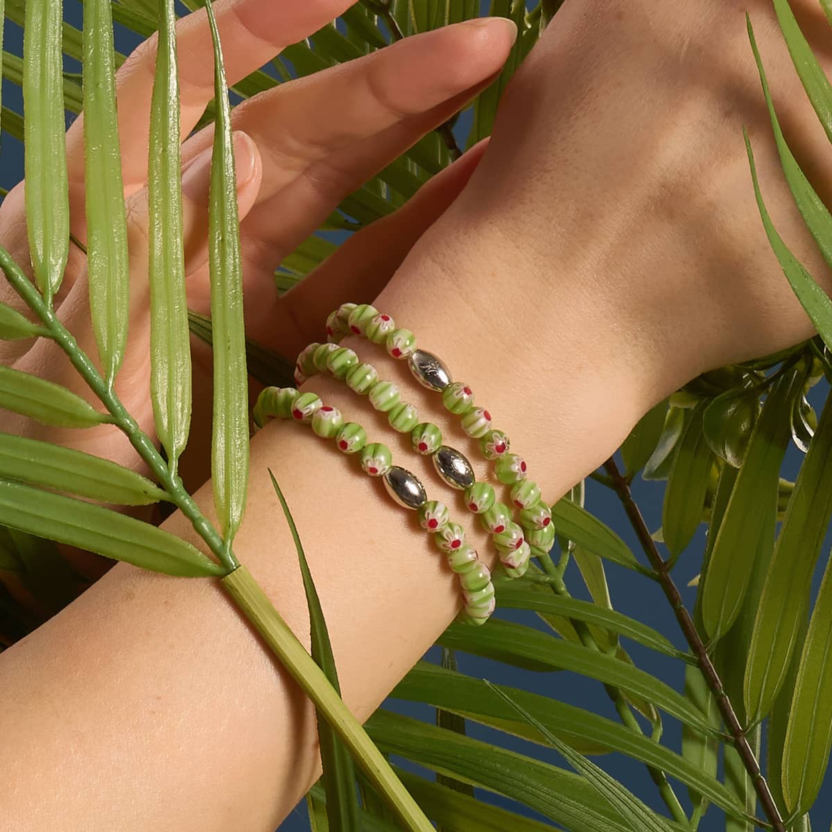 Sicilian Sage Millefiori Bracelet with green millefiori beads and .925 sterling silver logo charm on stretchable elastic cord worn by NOGU
