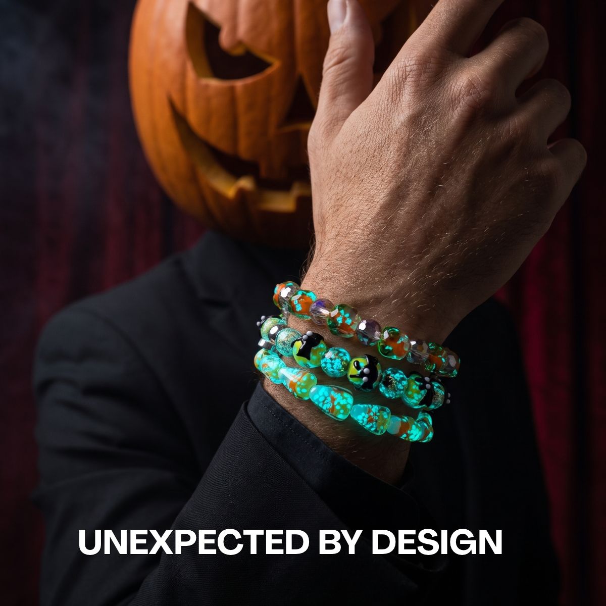 Stacked turquoise, orange and black beaded bracelets with playful Halloween motifs, worn with a black suit and pumpkin mask.