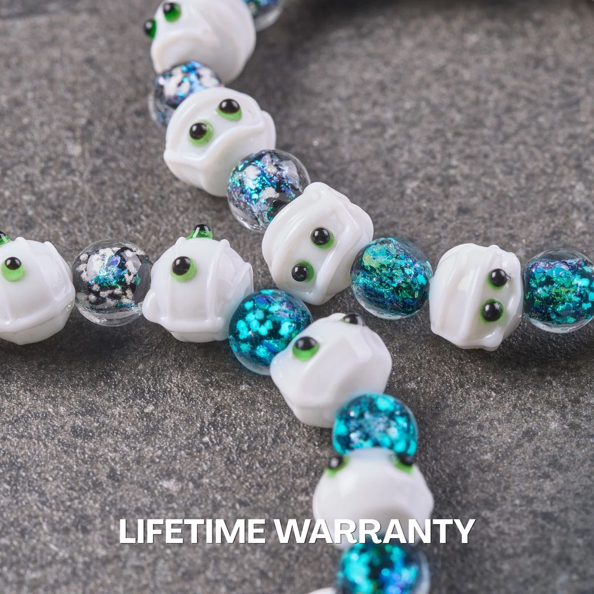 NOGU glass bead bracelet with white ghost faces and shimmering teal-blue foil beads in a playful Halloween style.