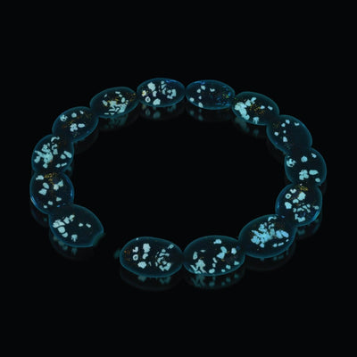 Pink Pony Club bracelet with glow-in-the-dark Firework Glass pebbles glowing blue in darkness, sterling silver base by NOGU