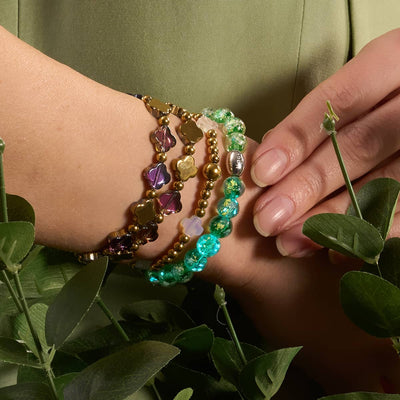 Verdant Burst bracelet with vibrant green Firework Glass beads and .925 sterling silver clasp layered with multicolor glass and gold bead bracelets on wrist by NOGU