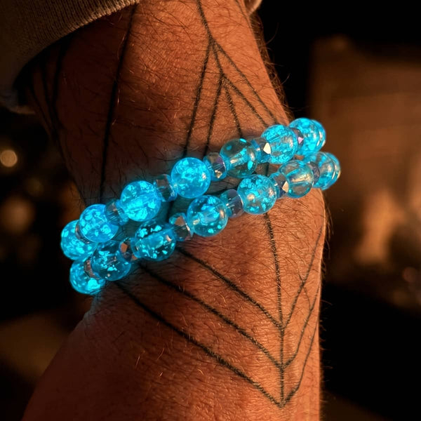 Aquamarine Ice Firefly Glass snow globe bracelet with luminous blue hand-blown glass beads and silver accents on a wrist.