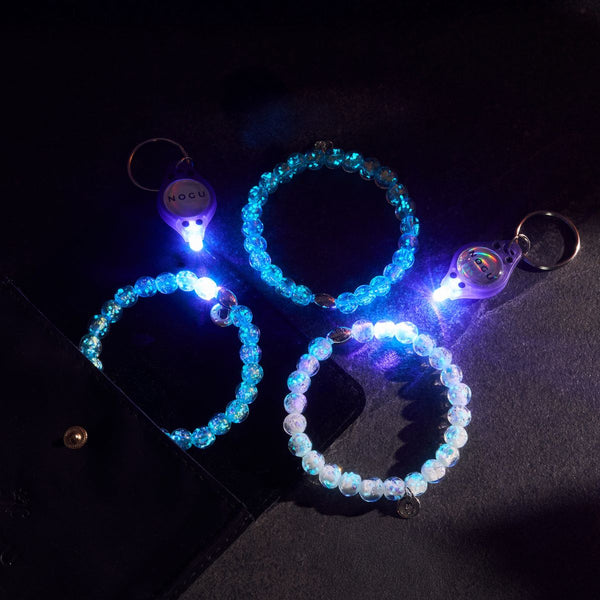 NOGU blue and white translucent beaded bracelets glow under UV light beside branded LED keychain lights.