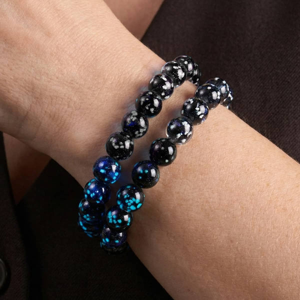 Pitch Black Firefly Glass bracelet with glossy black lampwork beads and vivid blue glowing flecks, worn on the wrist.