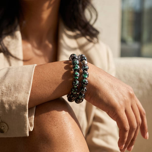 Aurora Borealis Firework Glass Orbit bracelet with dark silver beads and shimmering green accents on a clear elastic cord.