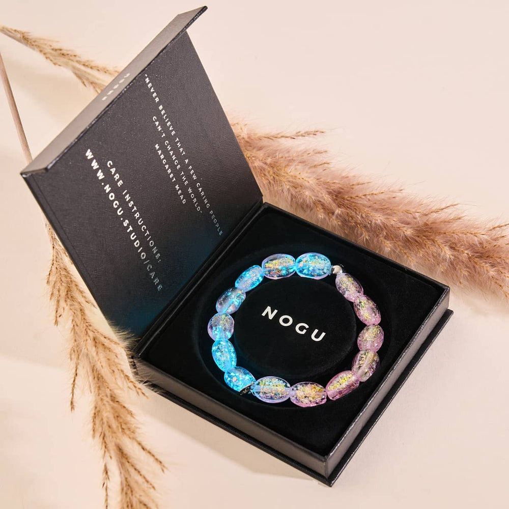 Pink Pony Club bracelet with iridescent blue and pink Firework Glass pebbles inside black NOGU box