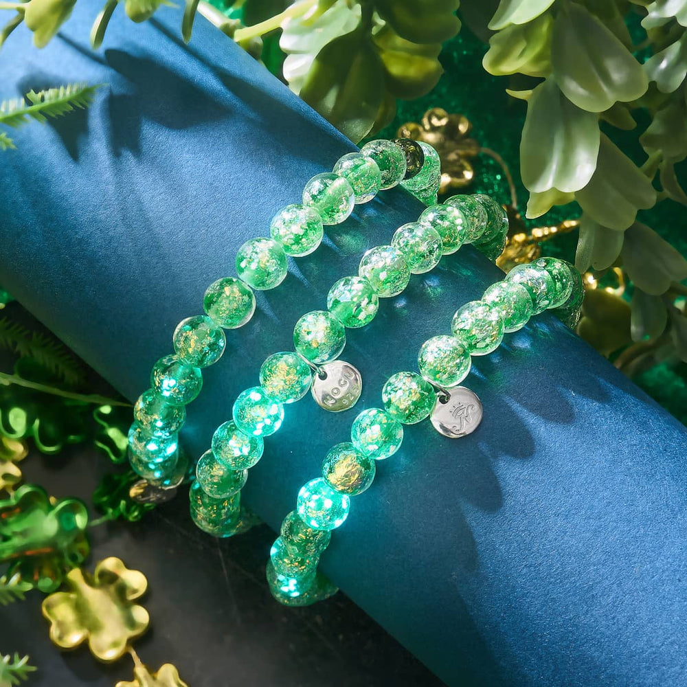 Verdant Burst bracelets with green and gold Firework Glass beads and .925 sterling silver charms displayed on a blue surface by NOGU